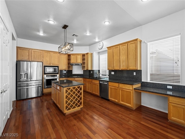 kitchen with a center island, built in desk, dark stone countertops, pendant lighting, and stainless steel appliances