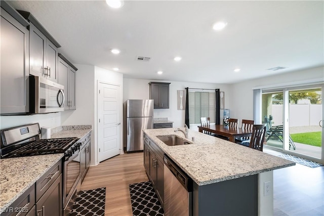 kitchen featuring sink, stainless steel appliances, light stone counters, light hardwood / wood-style floors, and an island with sink