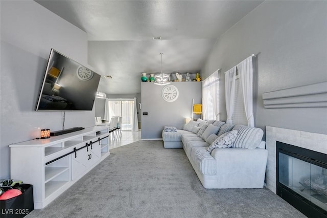 living room featuring an inviting chandelier, light colored carpet, vaulted ceiling, and a tile fireplace