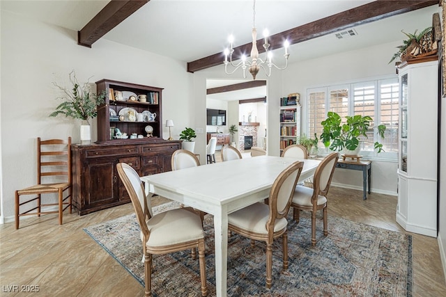 dining space with an inviting chandelier, a stone fireplace, and beamed ceiling