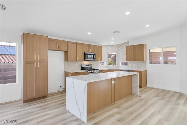 kitchen with light stone counters, a kitchen island, light hardwood / wood-style floors, and appliances with stainless steel finishes