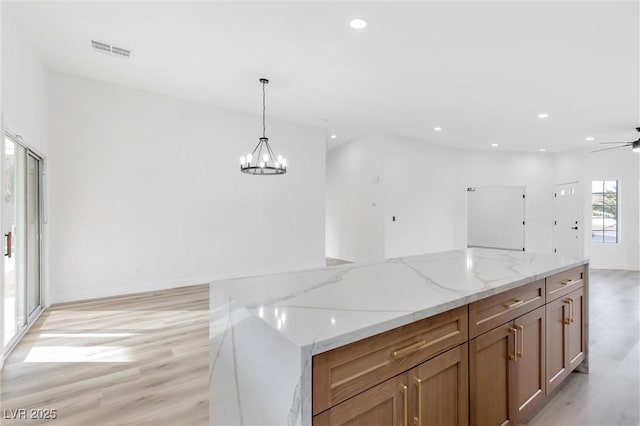 kitchen featuring pendant lighting, light hardwood / wood-style flooring, a spacious island, light stone counters, and ceiling fan with notable chandelier