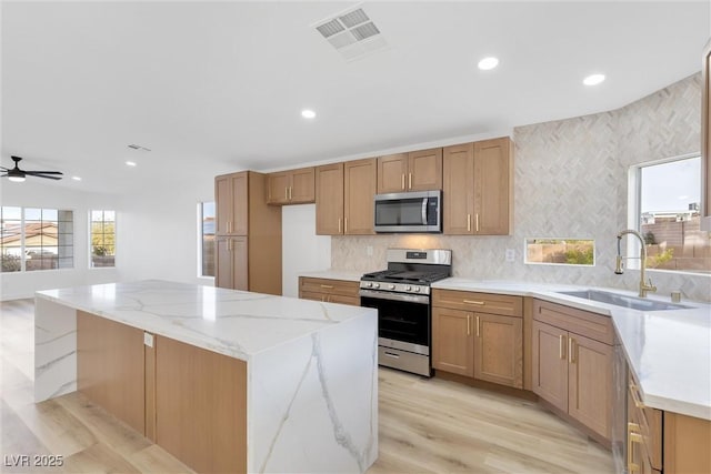 kitchen with sink, appliances with stainless steel finishes, light stone counters, light hardwood / wood-style floors, and a kitchen island