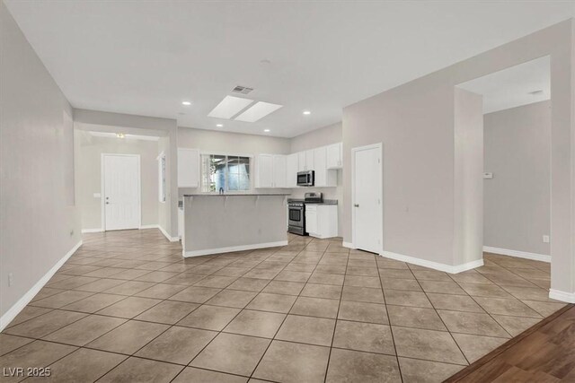 kitchen with light tile patterned floors, appliances with stainless steel finishes, a skylight, white cabinets, and kitchen peninsula