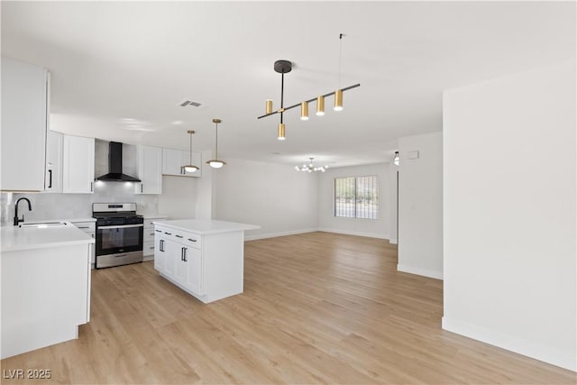 kitchen featuring a kitchen island, stainless steel stove, white cabinetry, hanging light fixtures, and wall chimney exhaust hood