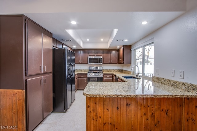 kitchen with sink, appliances with stainless steel finishes, kitchen peninsula, a raised ceiling, and light stone countertops