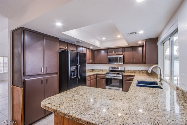 kitchen with appliances with stainless steel finishes, sink, kitchen peninsula, a raised ceiling, and light stone countertops