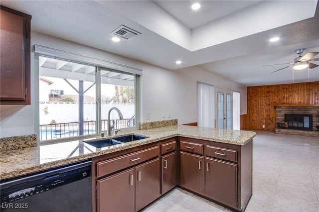 kitchen featuring a stone fireplace, sink, wood walls, dishwasher, and kitchen peninsula