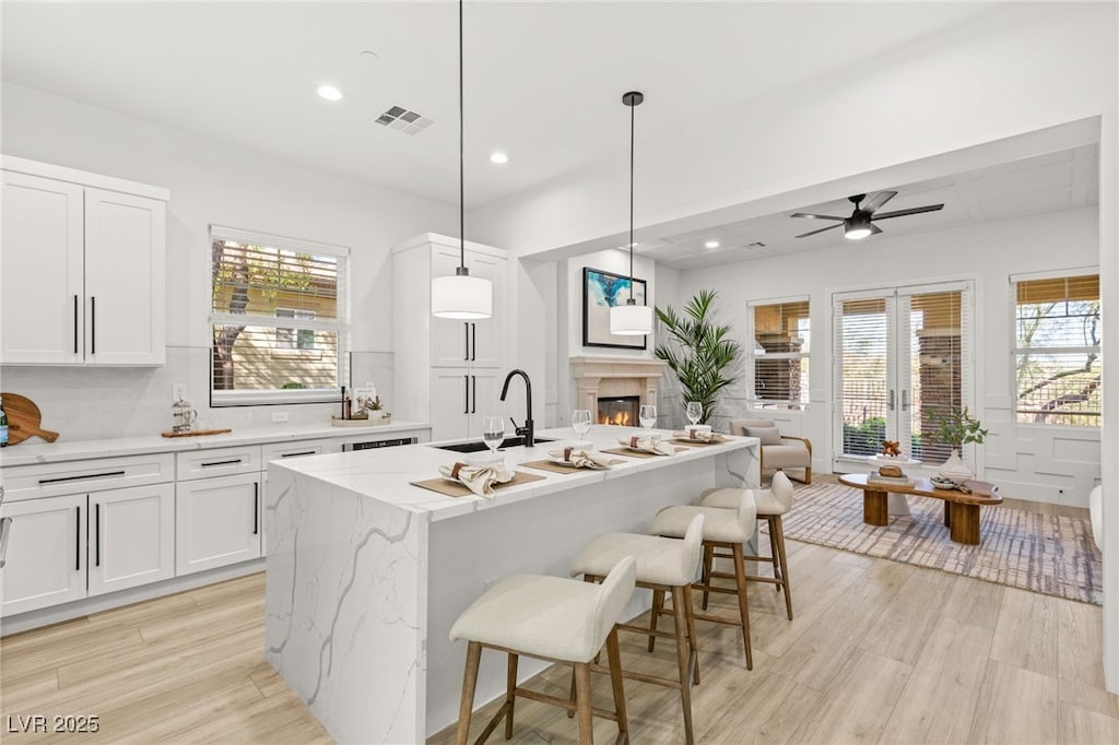 kitchen with sink, white cabinetry, a kitchen island with sink, hanging light fixtures, and light stone countertops