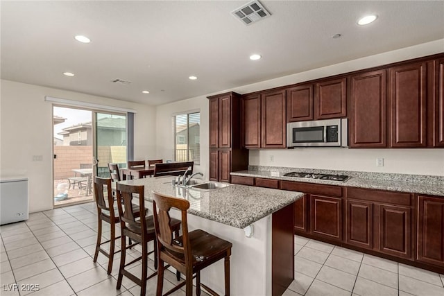 kitchen featuring sink, appliances with stainless steel finishes, a kitchen breakfast bar, an island with sink, and light stone countertops