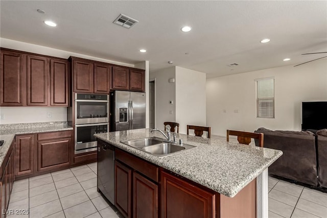 kitchen with sink, light tile patterned floors, stainless steel appliances, light stone countertops, and a kitchen island with sink