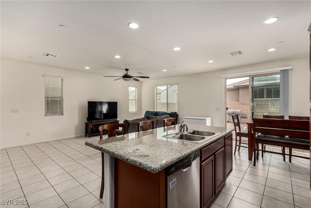 kitchen with dishwasher, an island with sink, sink, light tile patterned floors, and light stone counters