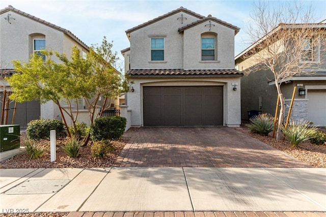 mediterranean / spanish-style home with a tiled roof, decorative driveway, an attached garage, and stucco siding