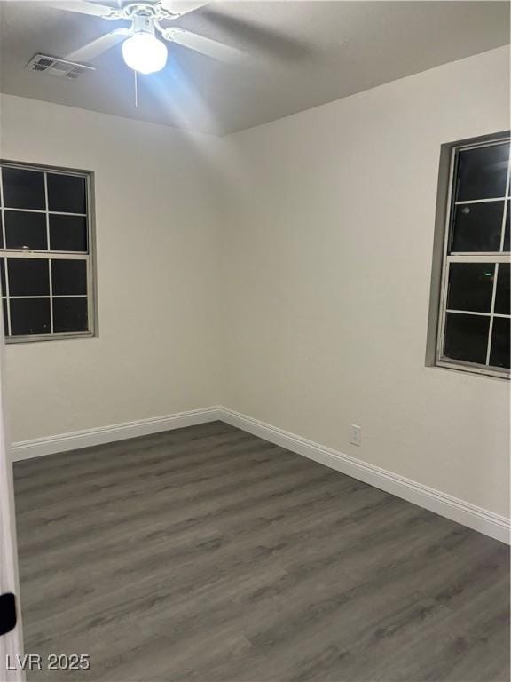 spare room with a ceiling fan, dark wood finished floors, visible vents, and baseboards