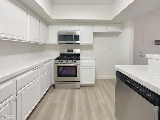 kitchen featuring white cabinetry, stainless steel appliances, a tray ceiling, and light hardwood / wood-style flooring