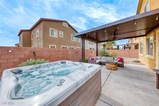 view of patio with ceiling fan, a hot tub, and an outdoor living space with a fire pit