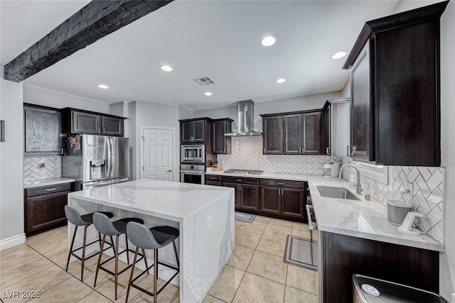 kitchen with wall chimney exhaust hood, sink, a center island, appliances with stainless steel finishes, and decorative backsplash