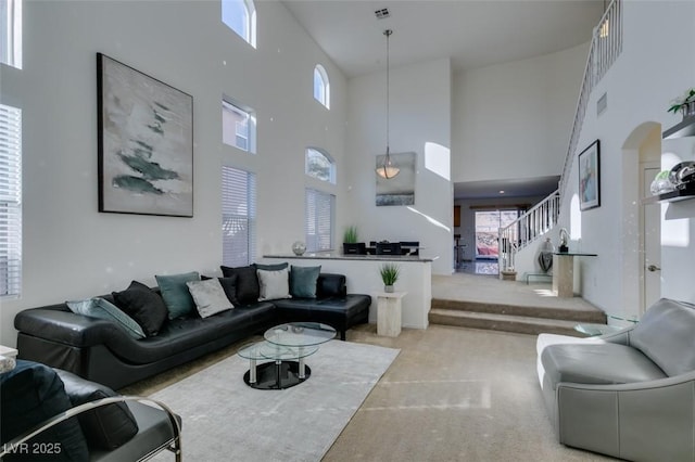 living area featuring arched walkways, light carpet, a high ceiling, visible vents, and stairs