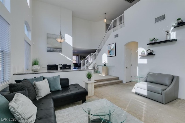 living room featuring a healthy amount of sunlight, a towering ceiling, and light colored carpet