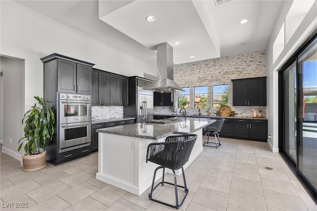 kitchen with island range hood, appliances with stainless steel finishes, a kitchen breakfast bar, a towering ceiling, and dark stone counters