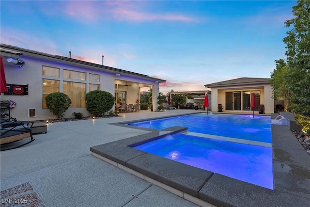 pool at dusk with a patio, pool water feature, and an in ground hot tub