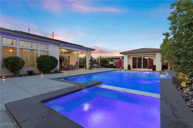 pool at dusk with an in ground hot tub and a patio