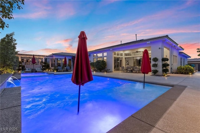 pool at dusk with pool water feature, ceiling fan, and a patio area