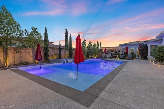 pool at dusk featuring pool water feature and a patio area