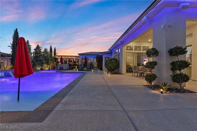 pool at dusk with pool water feature and a patio area