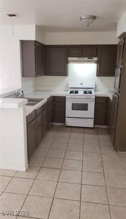 kitchen with stainless steel refrigerator, white range with gas cooktop, sink, and light tile patterned floors