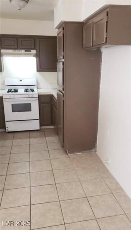 kitchen featuring light tile patterned floors, dark brown cabinets, and white gas stove