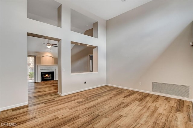 unfurnished living room featuring ceiling fan, a towering ceiling, and light hardwood / wood-style floors