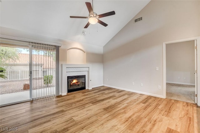 unfurnished living room featuring high vaulted ceiling, light hardwood / wood-style floors, a tile fireplace, and ceiling fan