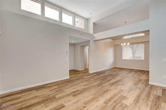 unfurnished room with a towering ceiling, a chandelier, and light wood-type flooring