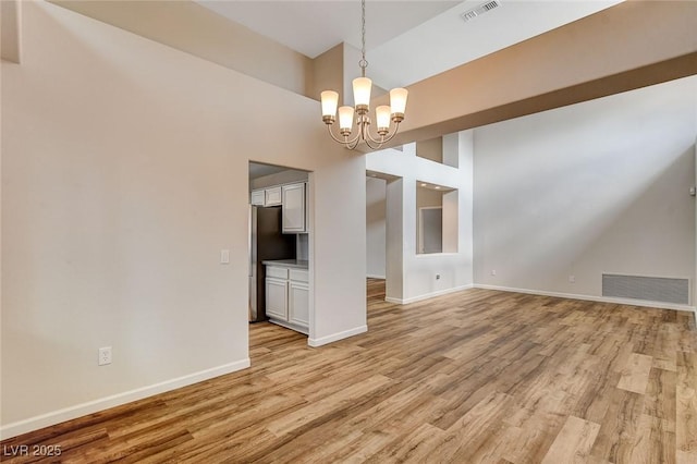 unfurnished dining area with an inviting chandelier, high vaulted ceiling, and light hardwood / wood-style floors