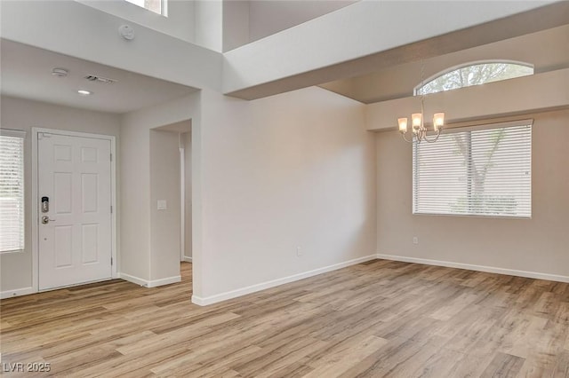 spare room featuring a notable chandelier, a wealth of natural light, and light wood-type flooring