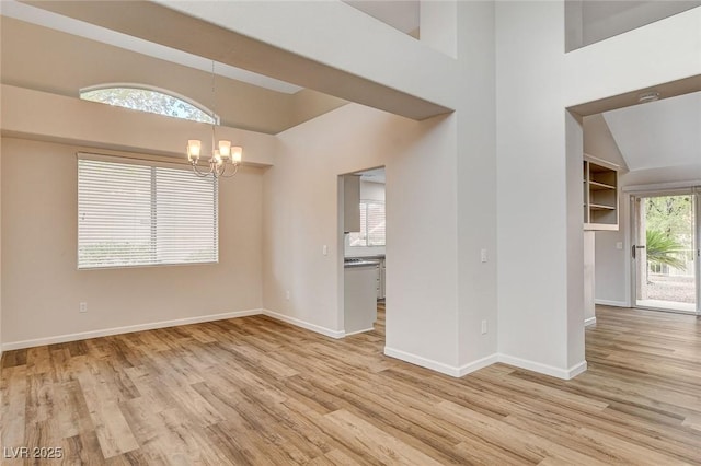 spare room with built in shelves, light hardwood / wood-style floors, and a chandelier