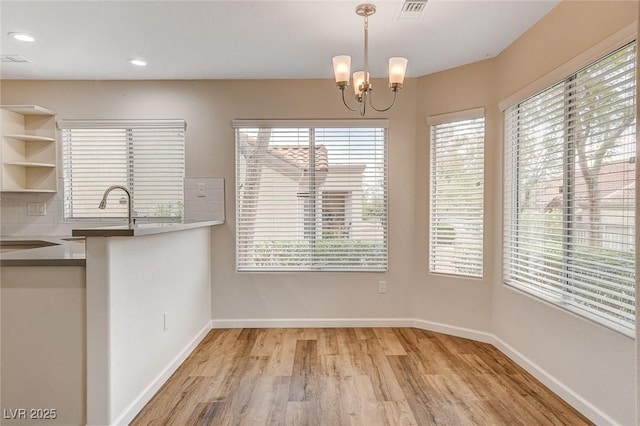 unfurnished dining area with sink, a notable chandelier, and light hardwood / wood-style floors