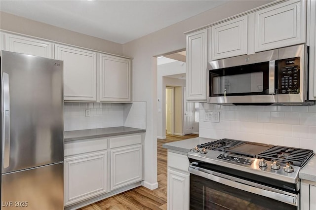 kitchen featuring white cabinetry, stainless steel appliances, light hardwood / wood-style flooring, and backsplash