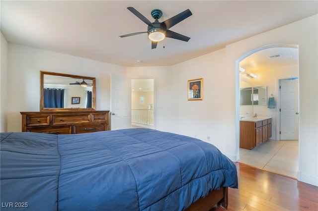 bedroom with arched walkways, light wood-type flooring, ensuite bathroom, visible vents, and a ceiling fan