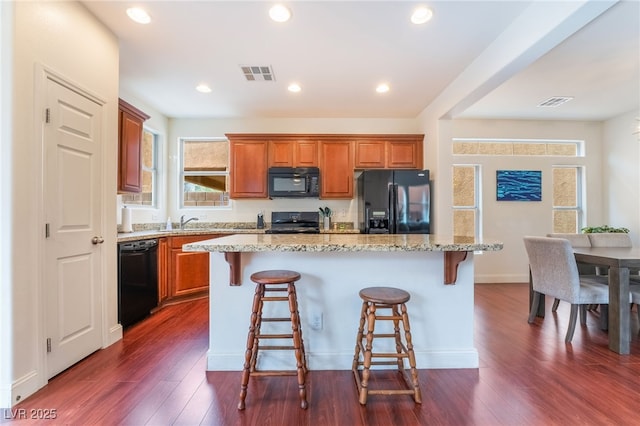 kitchen with a kitchen island, dark wood-type flooring, a breakfast bar area, and black appliances