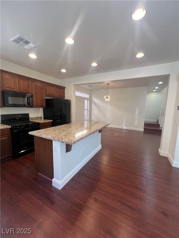 kitchen with dark wood finished floors, visible vents, light stone countertops, a breakfast bar, and black appliances