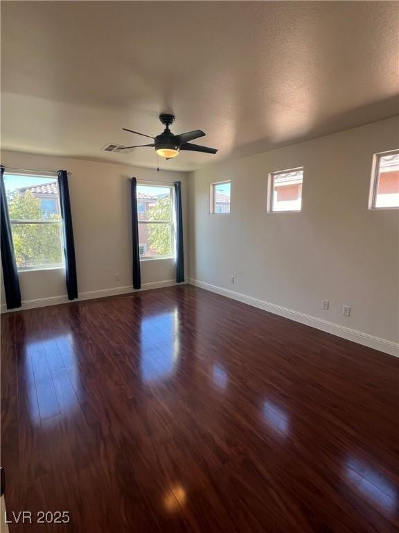 spare room featuring baseboards, dark wood-type flooring, and a wealth of natural light