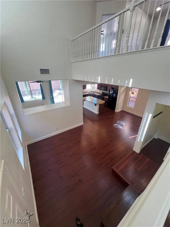 unfurnished living room with wood finished floors, a healthy amount of sunlight, a towering ceiling, and baseboards
