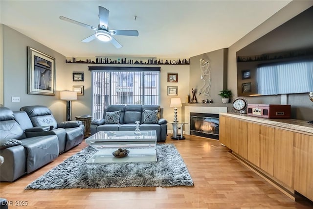 living room with a tile fireplace, light hardwood / wood-style floors, and ceiling fan