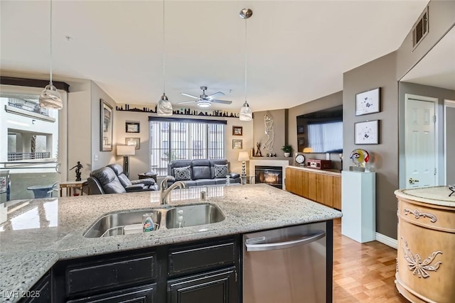 kitchen featuring sink, decorative light fixtures, light hardwood / wood-style flooring, dishwasher, and light stone countertops