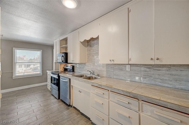 kitchen with sink, a textured ceiling, light wood-type flooring, appliances with stainless steel finishes, and decorative backsplash