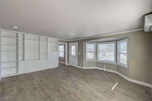 unfurnished living room featuring a wall unit AC, ornamental molding, and light wood-type flooring