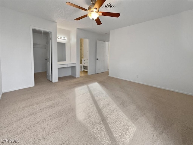 unfurnished bedroom with ensuite bathroom, a spacious closet, light colored carpet, ceiling fan, and a closet