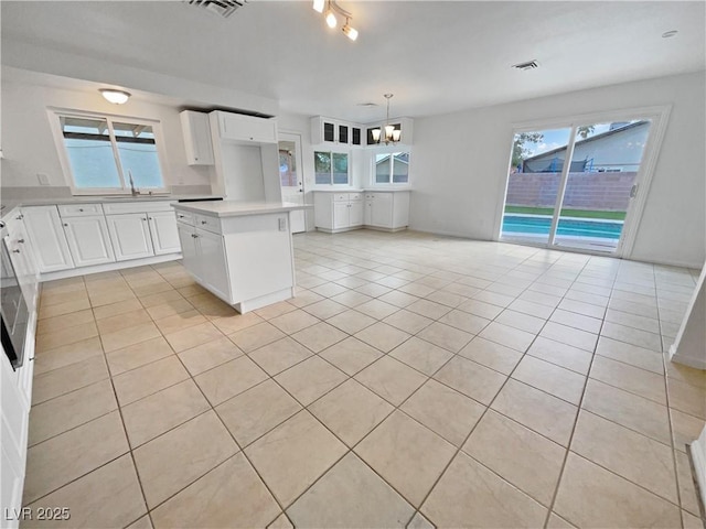 kitchen with light tile patterned floors, white cabinetry, a kitchen island, decorative light fixtures, and a chandelier